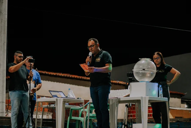 Apresentador com microfone e equipe ao lado do globo utilizado no sorteio da campanha